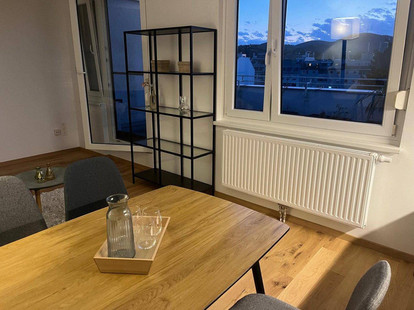 Heller Essbereich mit Holztisch, modernen Möbeln und Blick auf die Stadt bei Dämmerung.