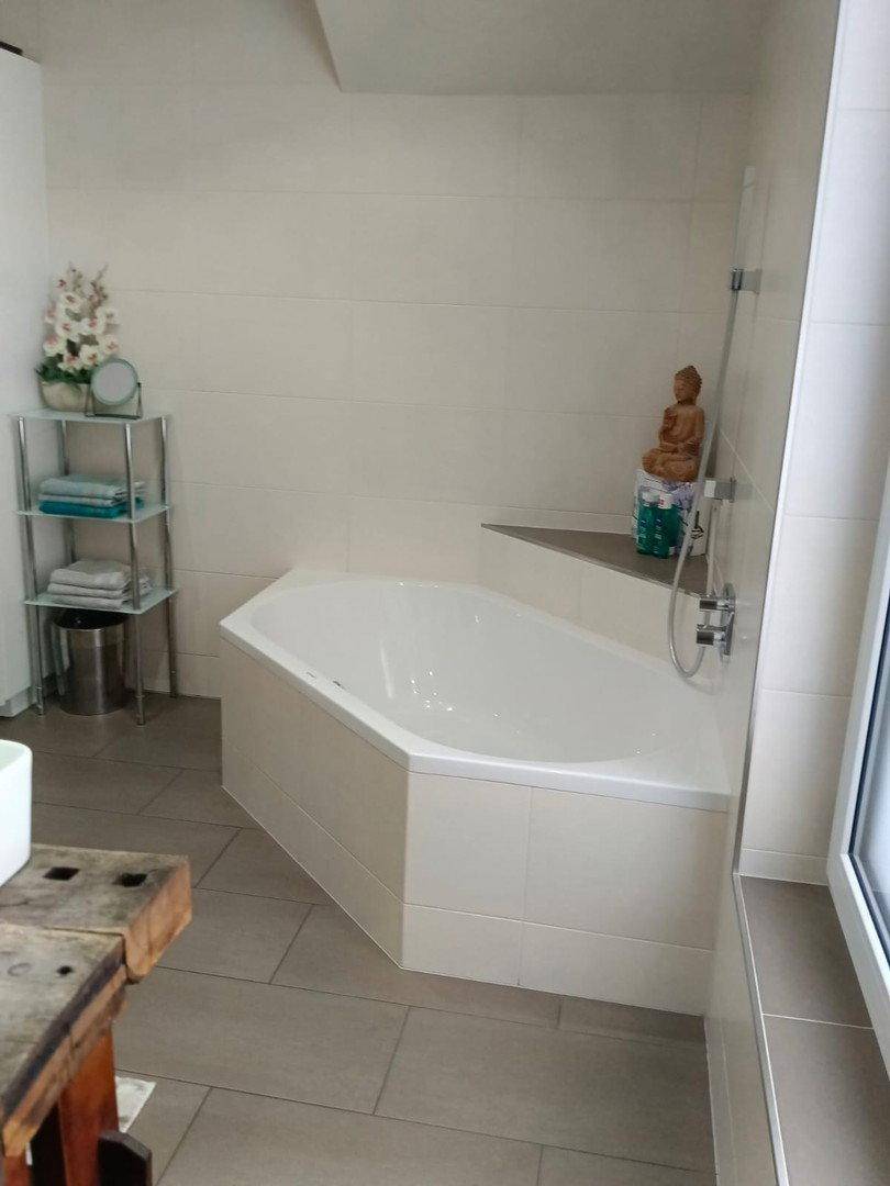 Helles Badezimmer mit Eckbadewanne und Duscharmatur, daneben ein rustikaler Holzschrank.