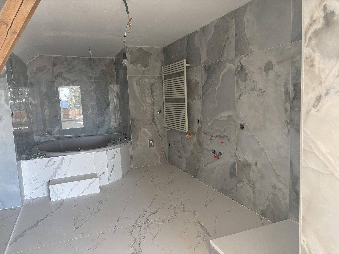 Geräumiges Badezimmer im Bau mit großen grauen Marmorfliesen und Eckbadewanne.