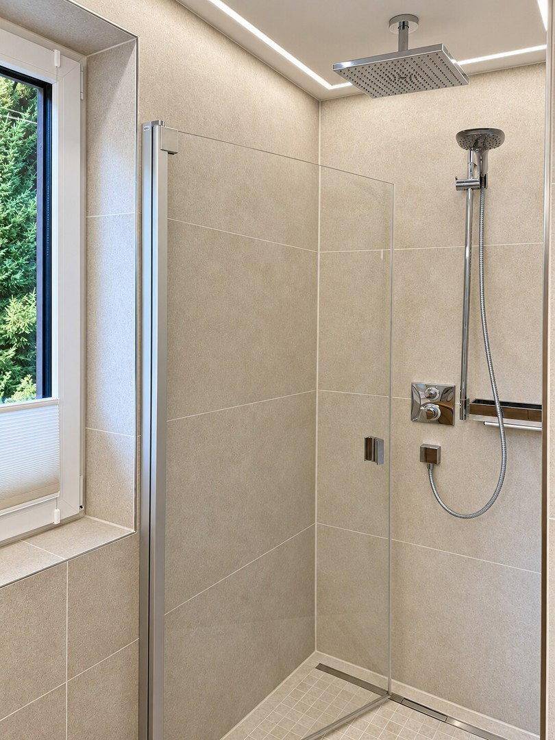 Geräumige Dusche mit Glasabtrennung, Regenduschkopf und modernen Armaturen in hellem Bad.