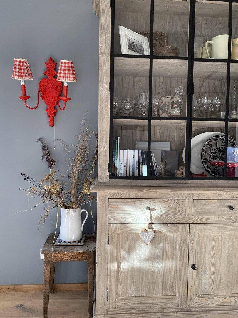 Detailansicht eines Holzschranks mit Glasvitrine und traditioneller Wandleuchte.