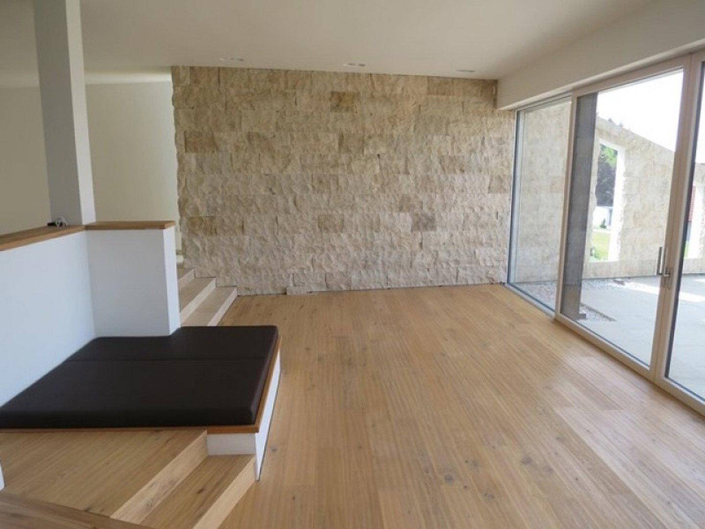 Geräumiger Wohnbereich mit Natursteinwand, großen Fenstern und Holzboden.