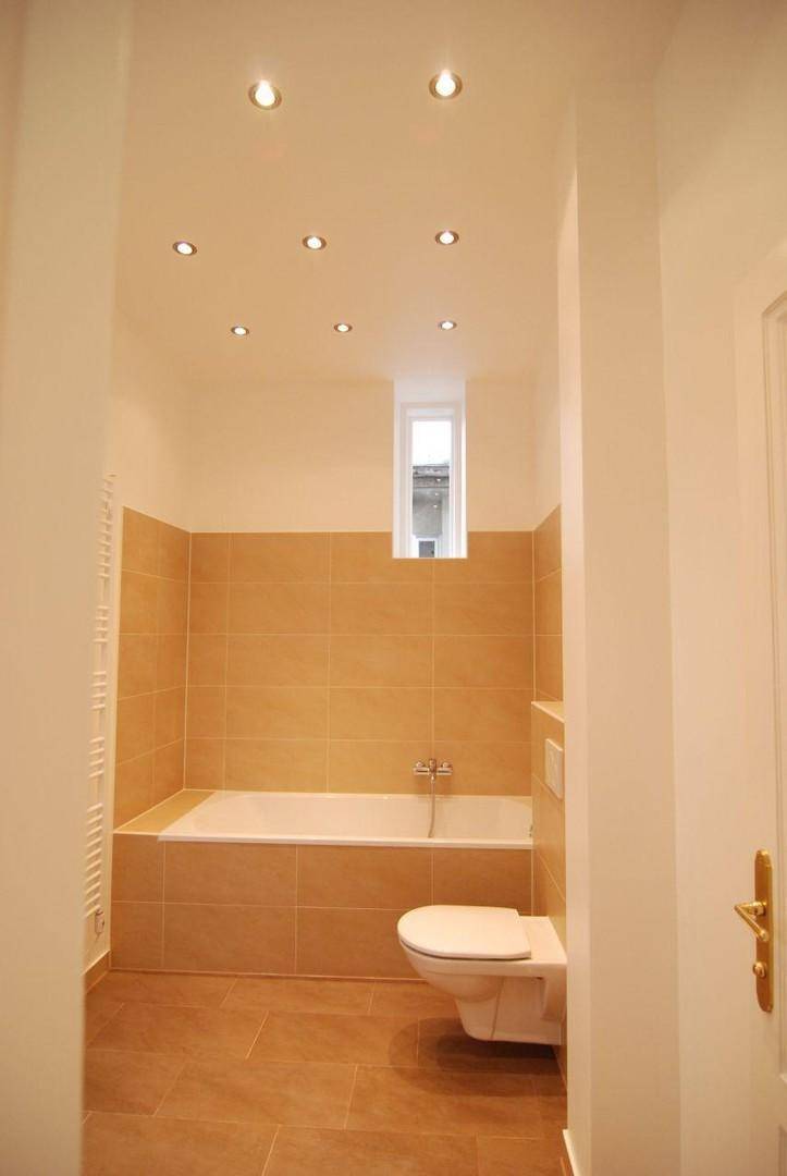 Modernes Badezimmer mit Badewanne, Wand-WC, beigefarbenen Fliesen und Einbaustrahlern.