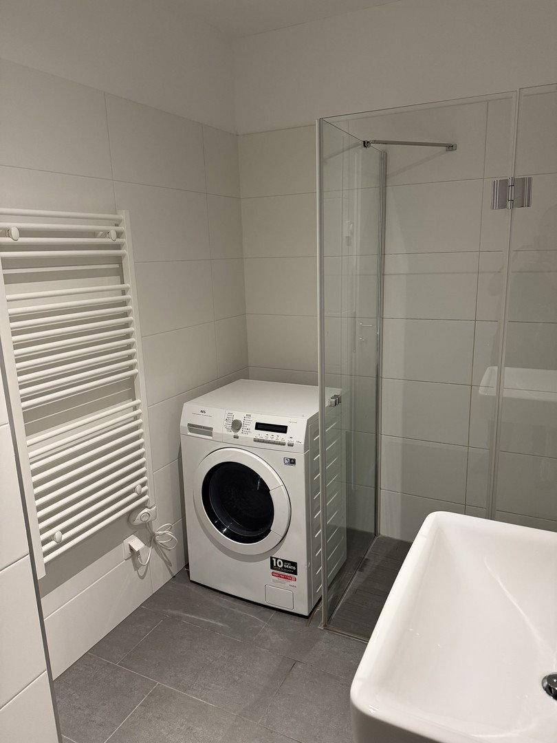 Helles Badezimmer mit Dusche, Waschmaschine und praktischem beheiztem Handtuchhalter.
