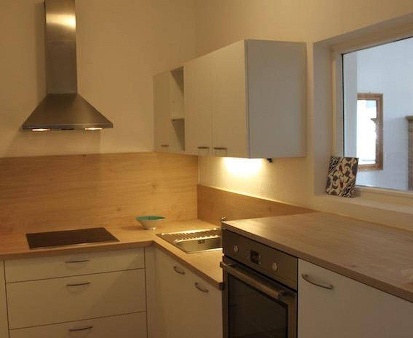 Moderne Küche mit weißen Schränken, Holzarbeitsplatten und integrierten Geräten, inklusive Fenster.