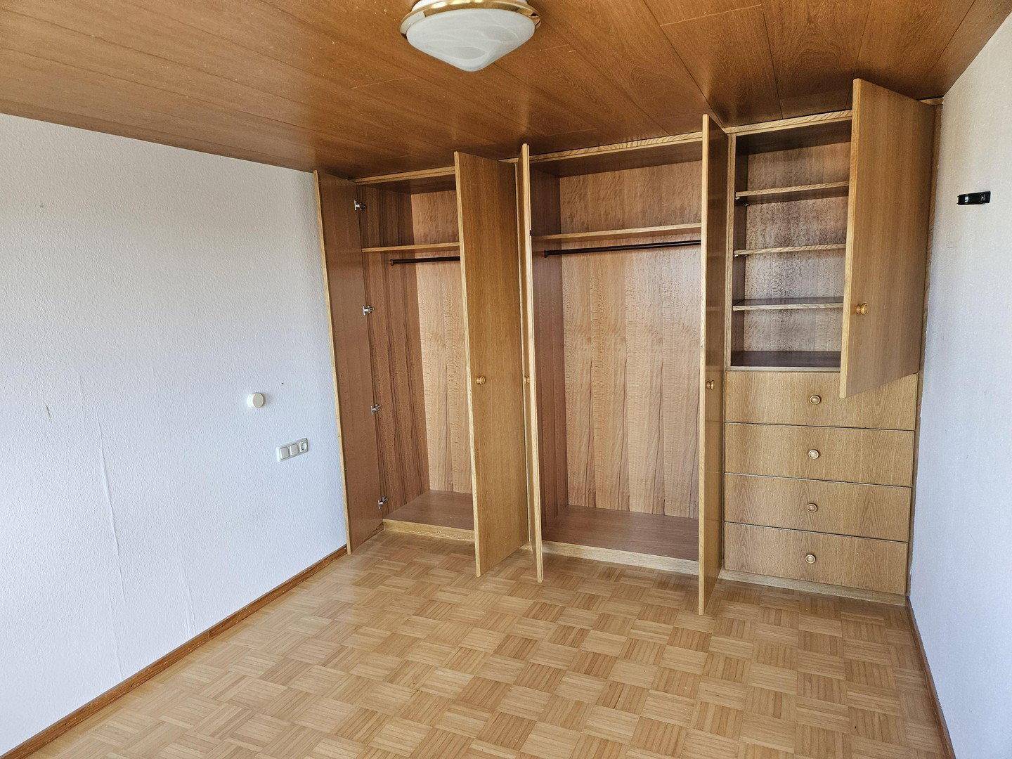 Geräumiges Schlafzimmer mit geöffneten Einbauschränken und klassischem Parkettboden.
