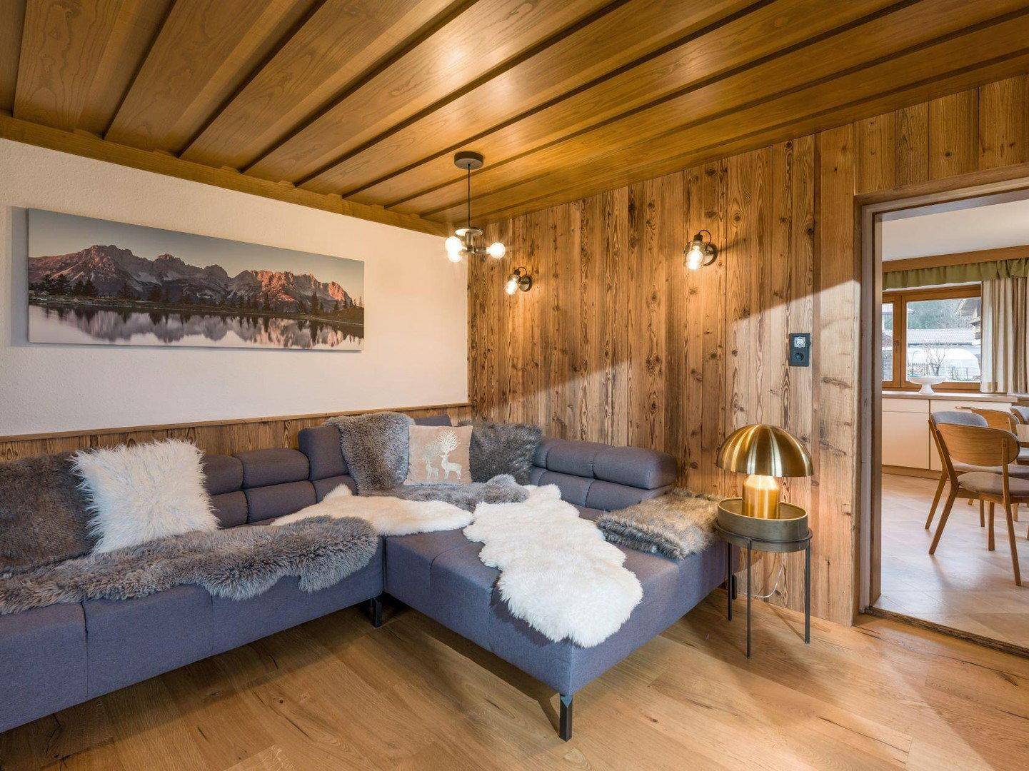Gemütliches Wohnzimmer mit Holzwänden, großem Ecksofa und Holzbalkendecke.