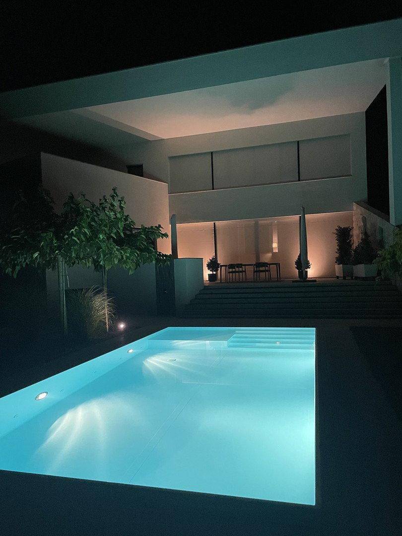 Beleuchtetes modernes Haus und Poolbereich bei Nacht, schafft eine stimmungsvolle Atmosphäre.