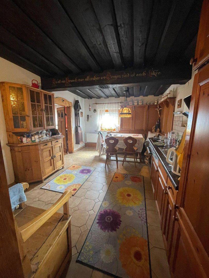 Rustikale Küche mit Holzbalkendecke, traditionellen Holzmöbeln und Essbereich am Fenster.