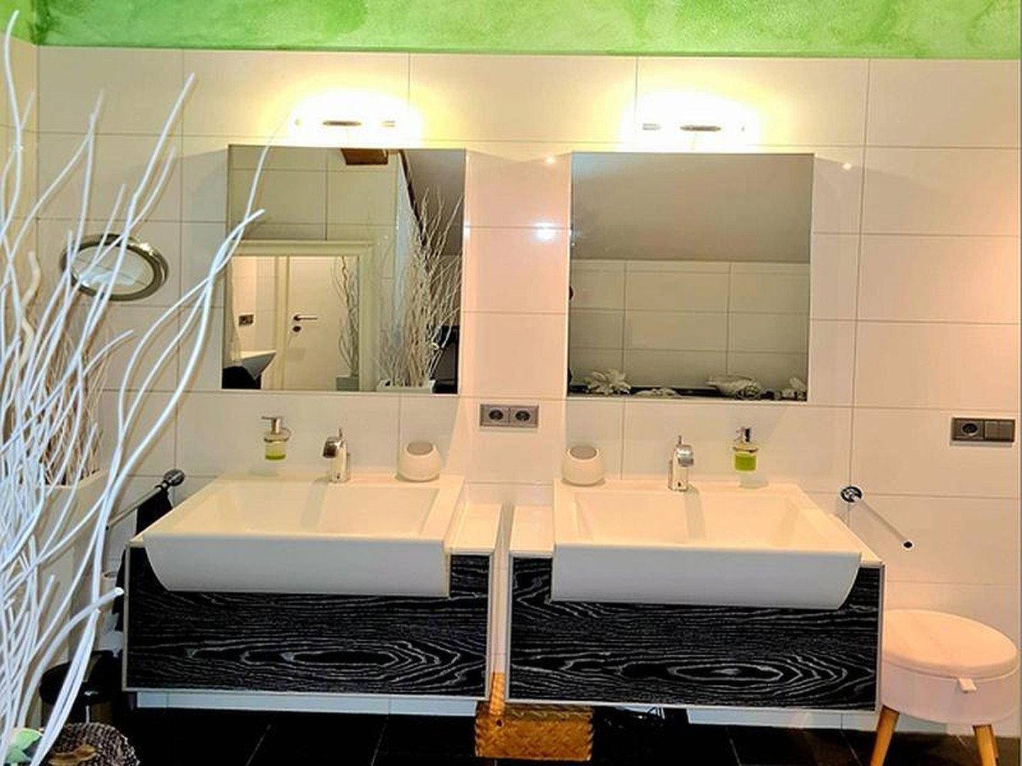 Modernes Badezimmer mit Doppelwaschbecken, weißen Fliesen und dunklen Möbeln.