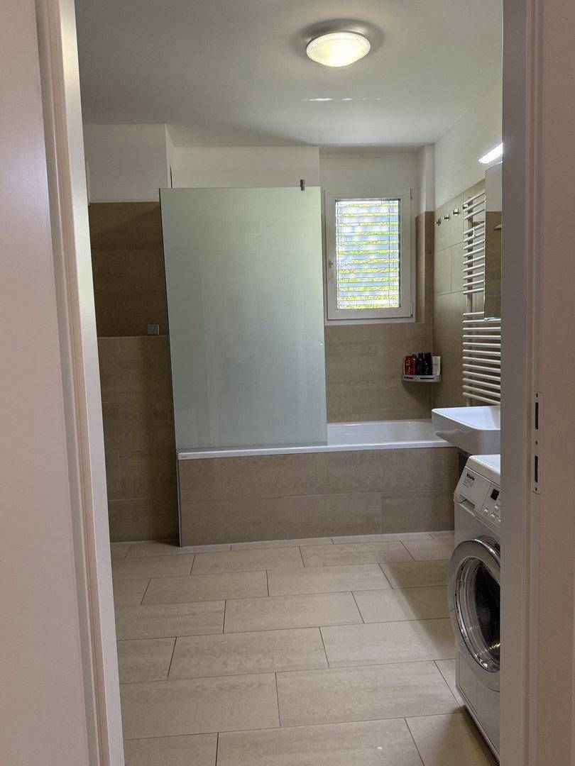 Modernes Badezimmer mit Badewanne, Glasabtrennung, Waschmaschine und beheiztem Handtuchhalter.