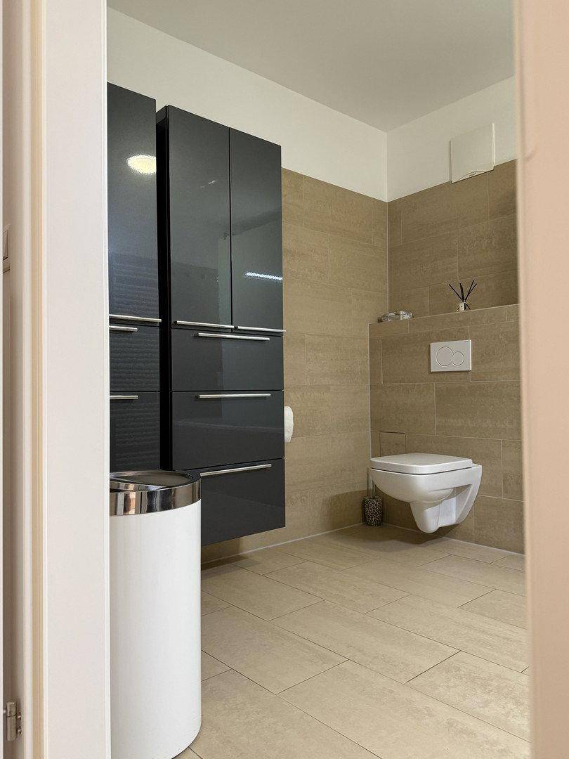 Modernes WC mit wandhängender Toilette, eleganten grauen Schränken und Fliesenboden.
