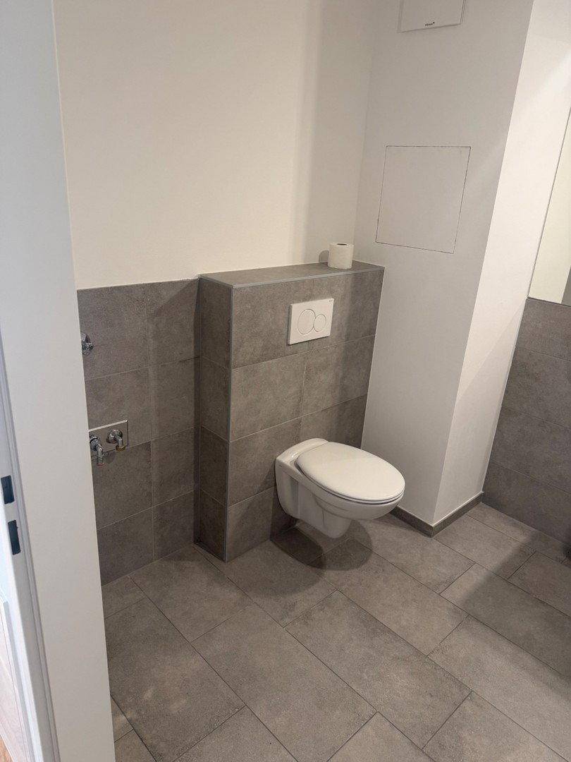 Separates WC mit modernen grauen Fliesen und wandhängender Toilette.
