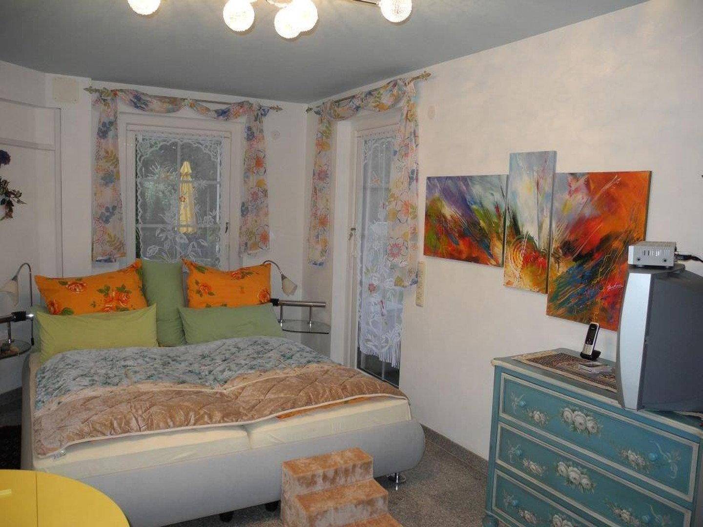 Schlafzimmer mit Doppelbett, farbenfroher Kunst und Zugang zu einem kleinen Balkon.