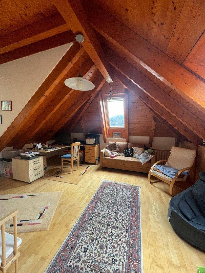 Funktionaler Dachbodenraum mit Schreibtisch, Sitzecke und Holzbalken unter schräger Decke.