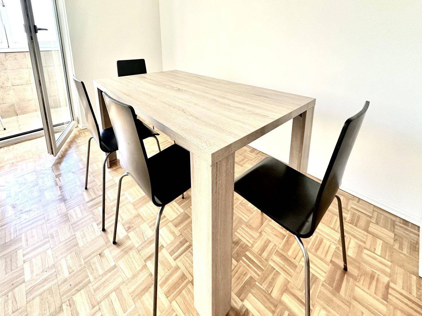 Heller Essbereich mit modernem Holztisch und schwarzen Stühlen, direkt am Balkonzugang gelegen.