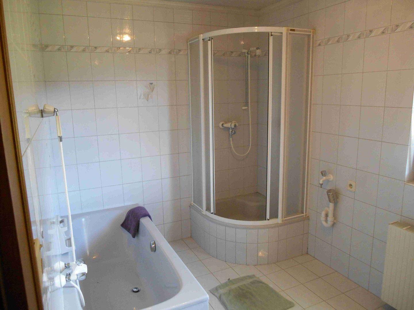 Helles Badezimmer mit Badewanne, Duschkabine und weißen Fliesen an Wänden und Boden.