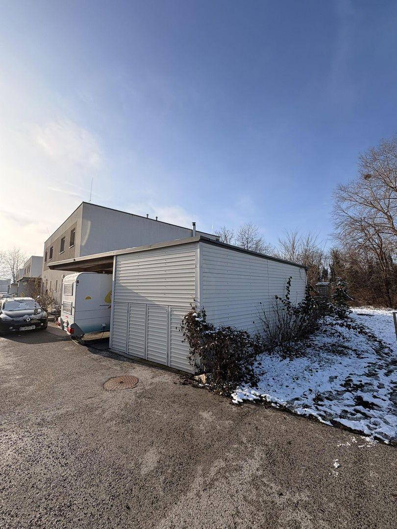 Seitenansicht des Gebäudes mit Carport und einem Nebengebäude, umgeben von Schnee.