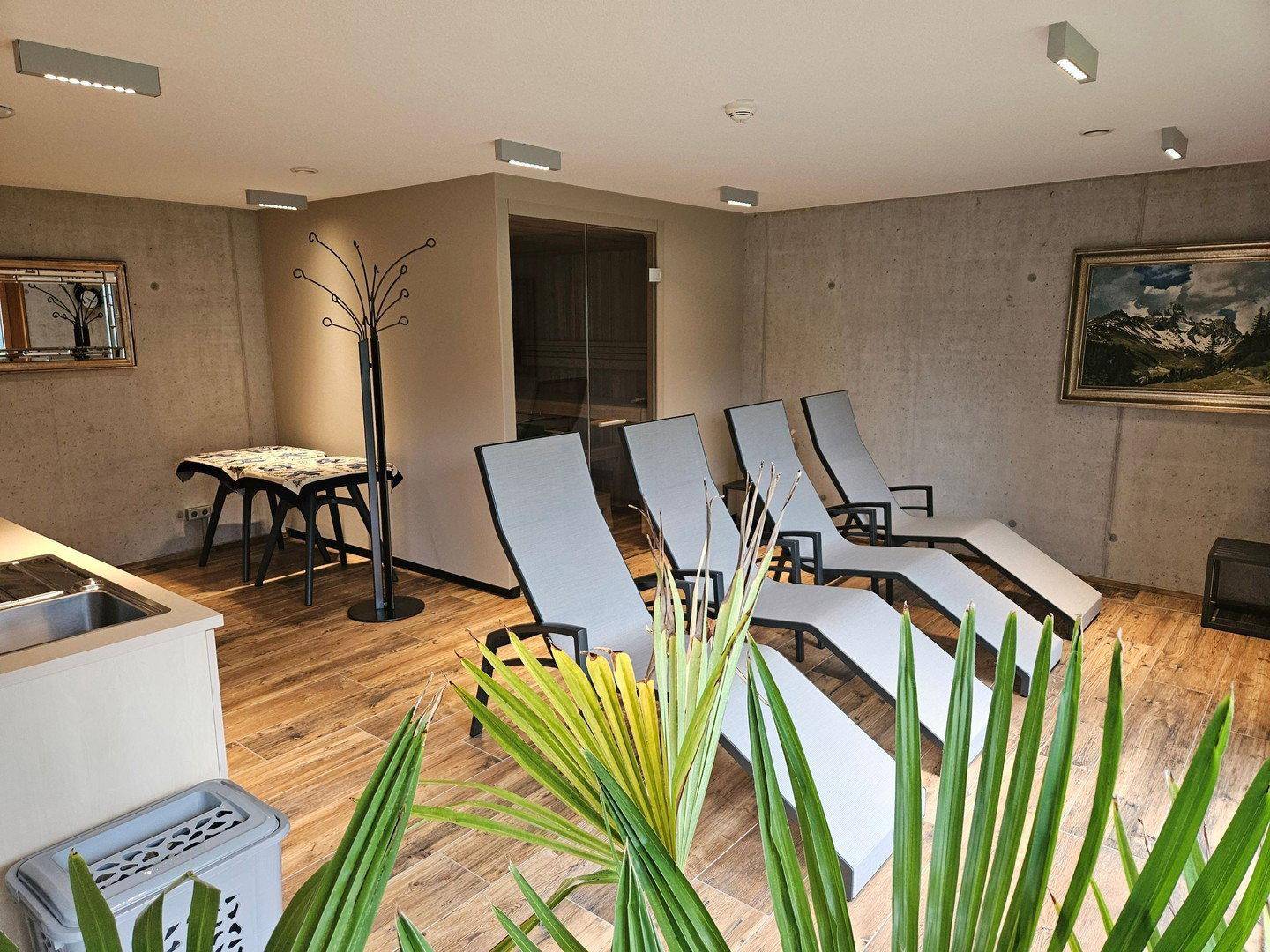 Wellnessbereich mit Liegestühlen, Holzboden und einer sichtbaren Sauna für Entspannung.