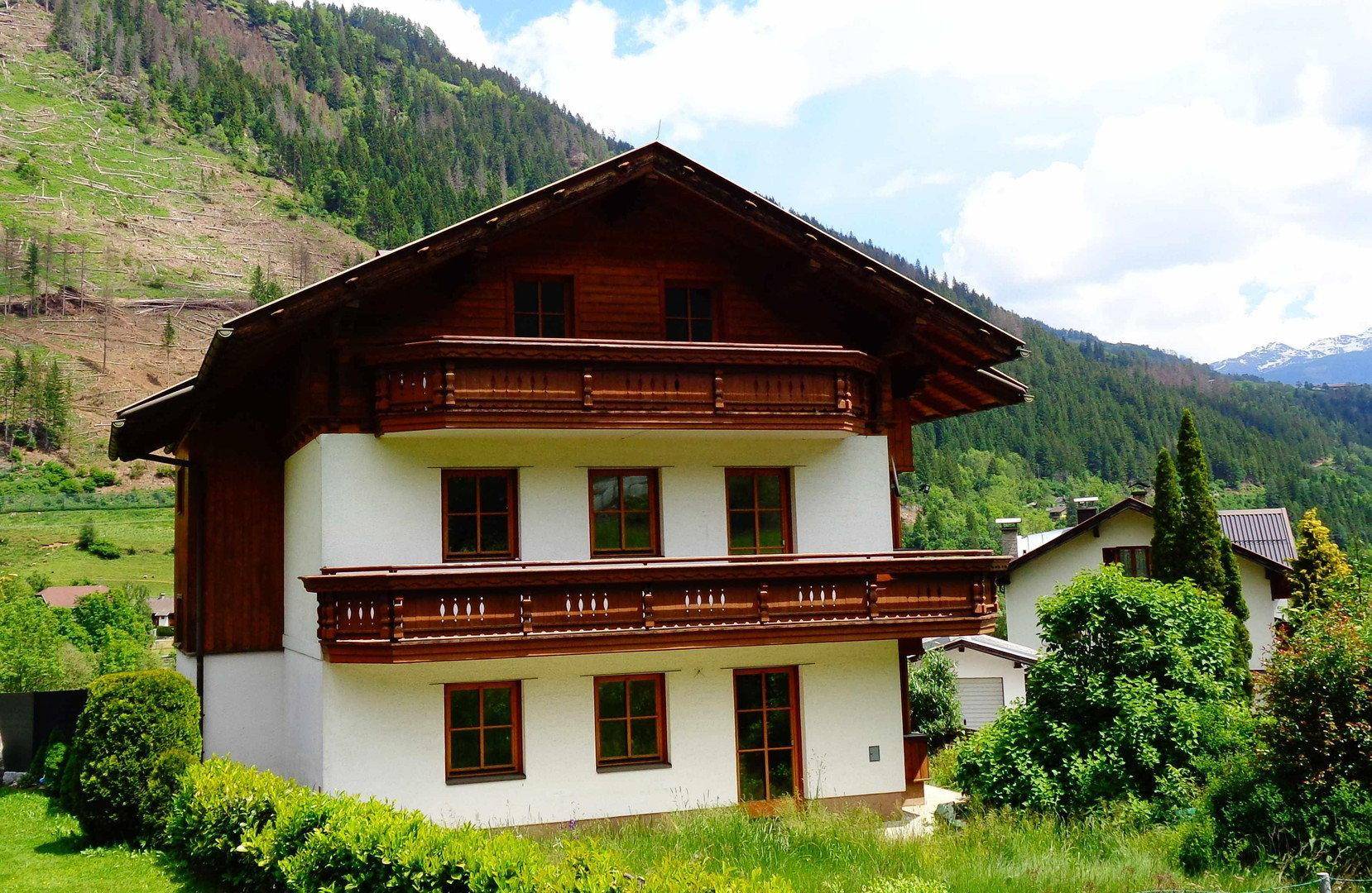 Traditionelles Haus im alpinen Stil mit Holzbalkonen und Bergblick in grüner Umgebung.