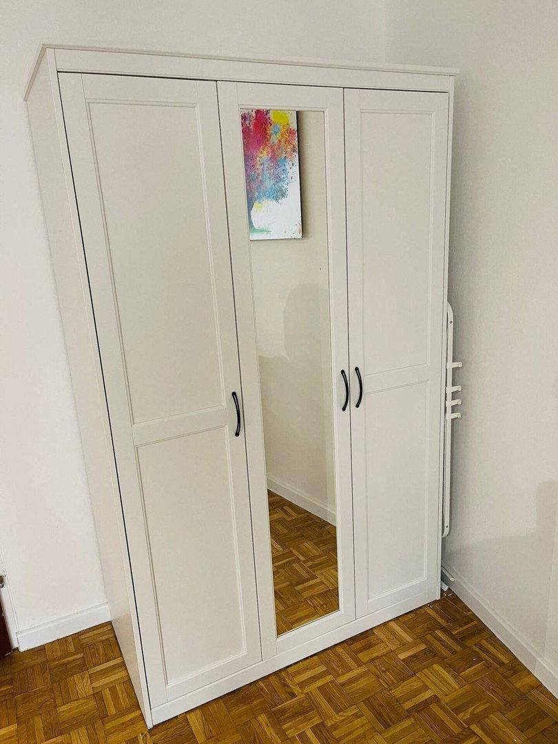 Weißer Kleiderschrank mit Spiegeltür in einem Raum mit Parkettboden.