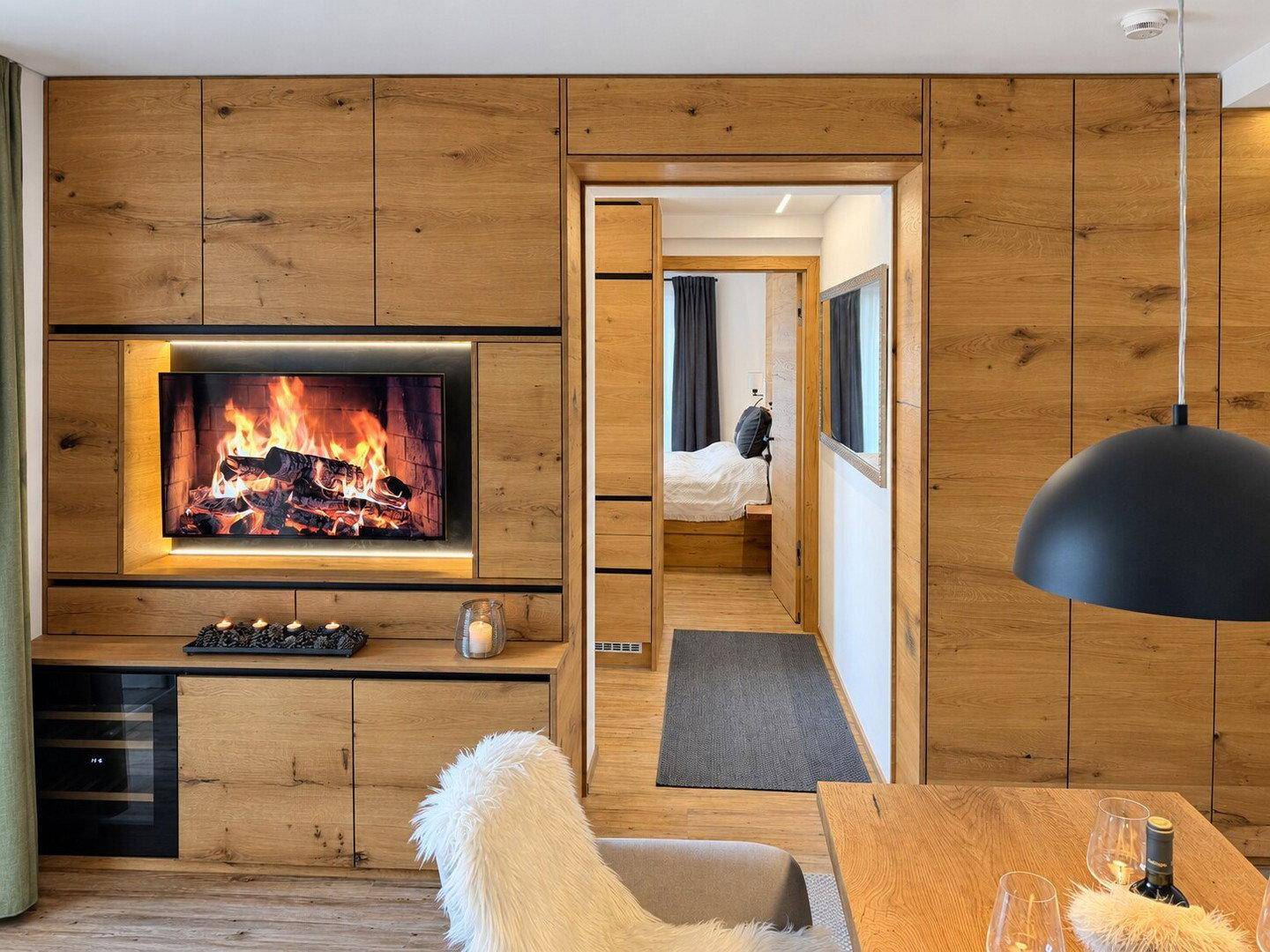 Moderner Wohnbereich mit Holzwandverkleidung, integriertem TV und Zugang zu einem Schlafzimmer.