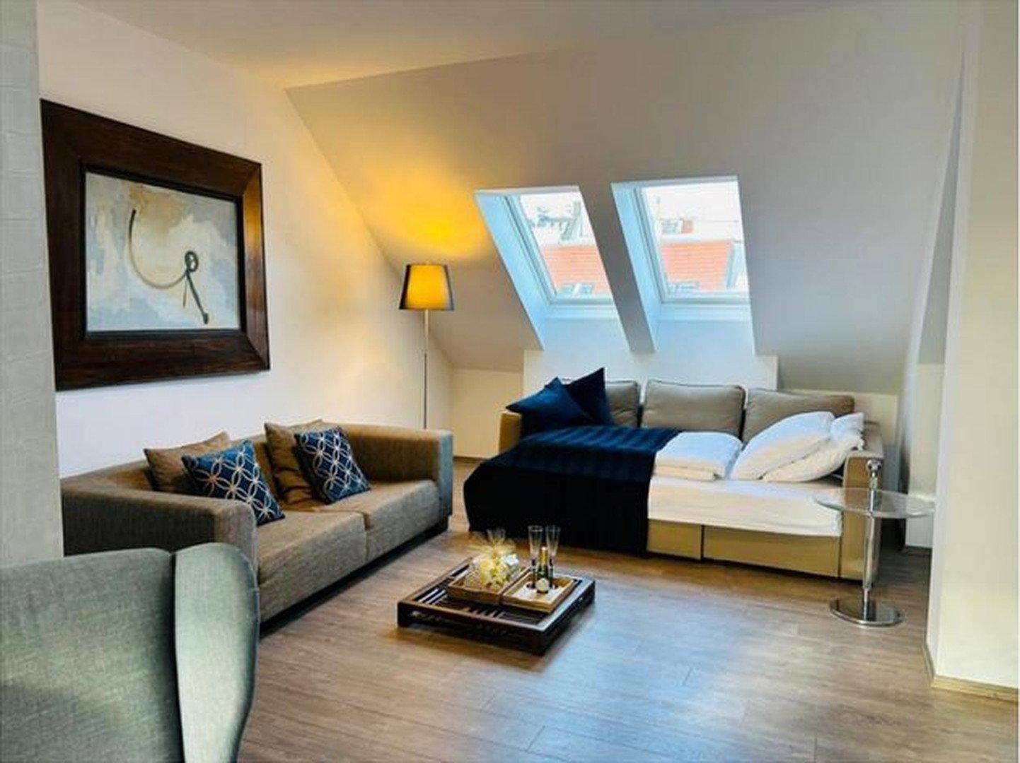 Gemütlicher Wohnbereich im Dachgeschoss mit bequemer Couch, Stehlampe und zwei Dachfenstern.