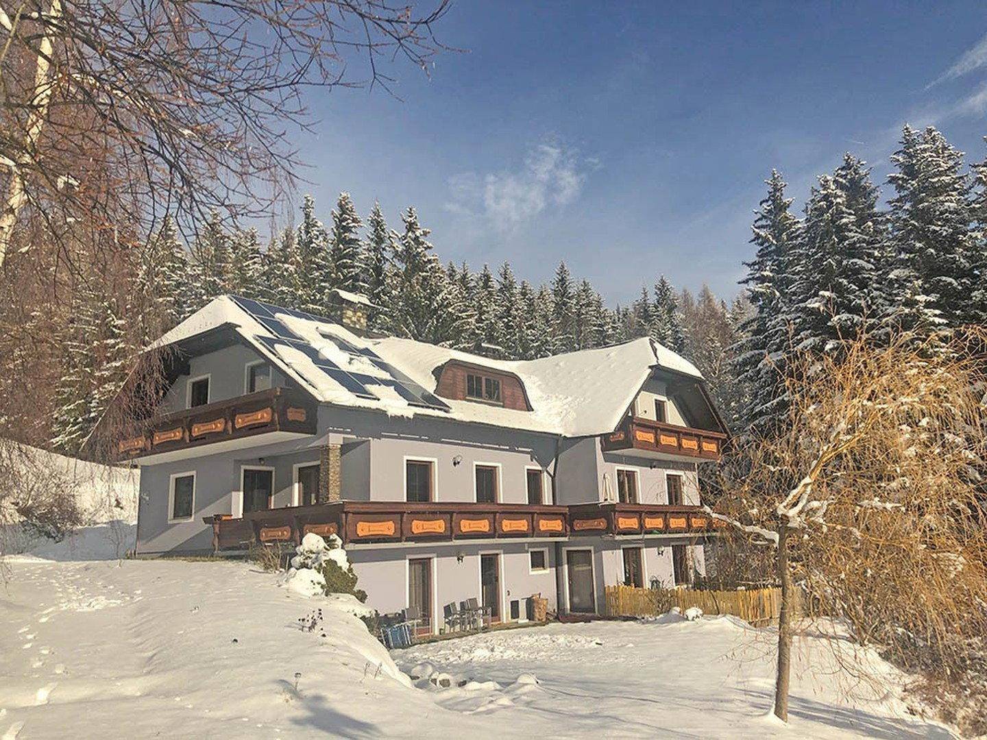 Haus mit Solaranlage und Balkonen, eingebettet in eine verschneite Winterlandschaft.