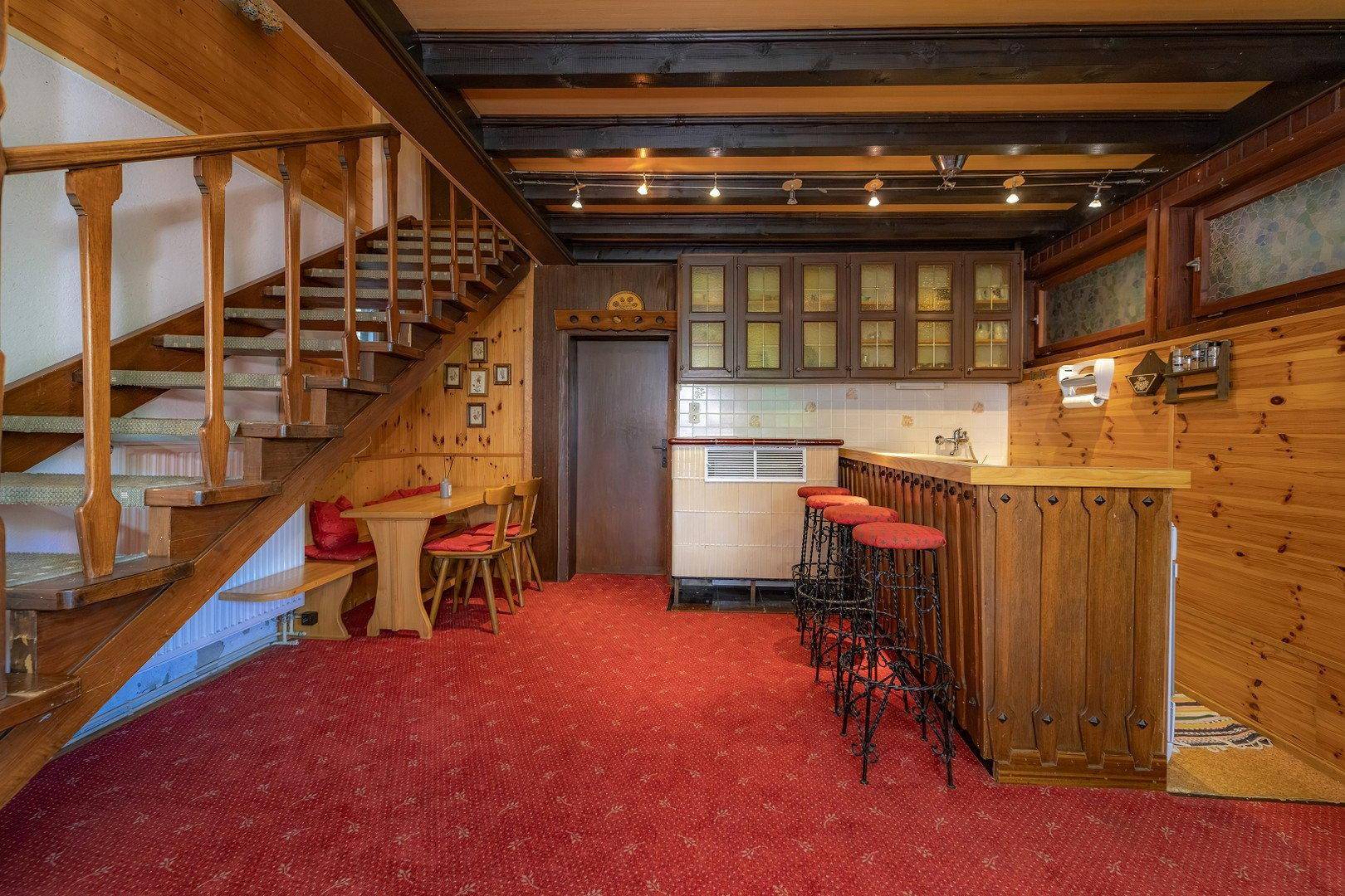 Rustikaler Wohnbereich mit Holzvertäfelung, einer Bar und einer Treppe, die nach oben führt.