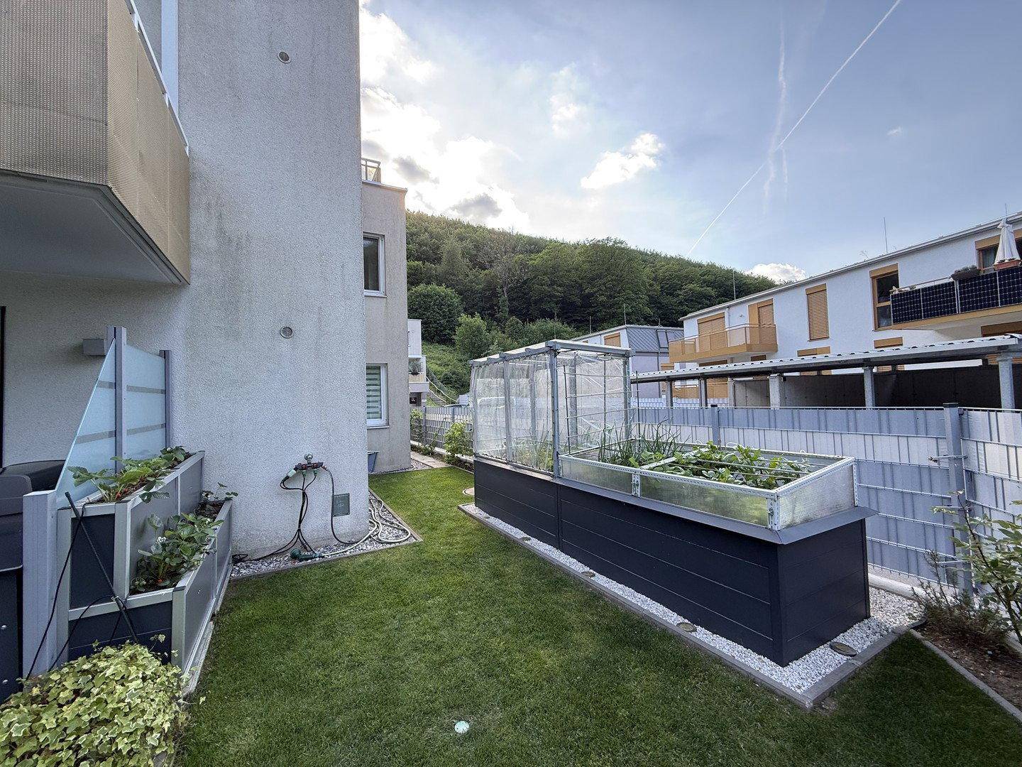 Garten mit Hochbeeten und einem kleinen Gewächshaus, ideal für den Anbau von Gemüse.