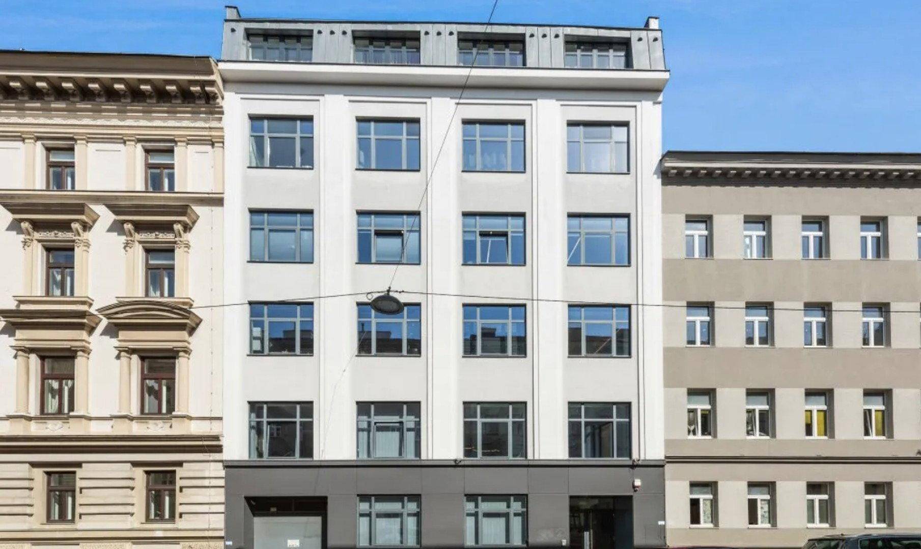 Moderne Gebäudefassade mit vielen Fenstern und klaren Linien, umgeben von städtischer Architektur.