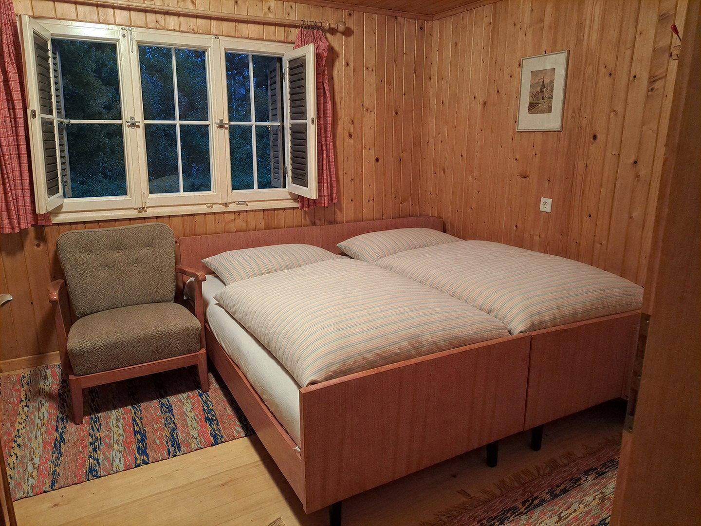 Ruhiges Schlafzimmer mit Holzboden, Holzvertäfelung und einem bequemen Sessel.