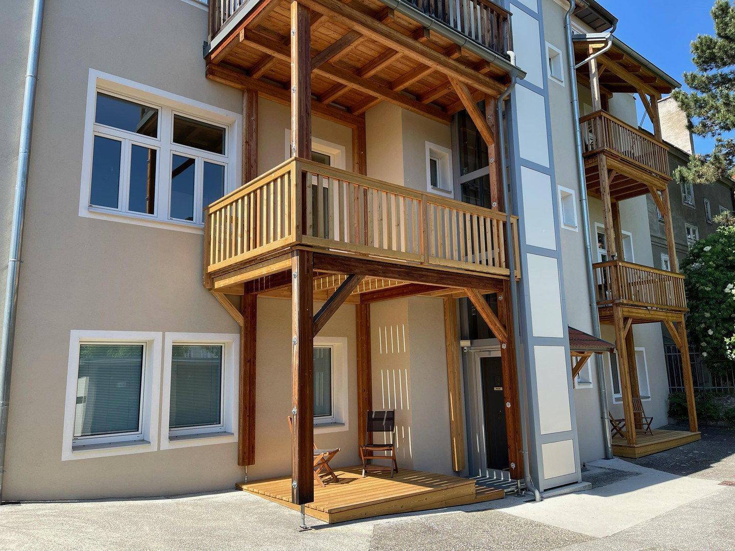 Seitenansicht des Gebäudes mit neuen Holz-Balkonen und externem Aufzug.