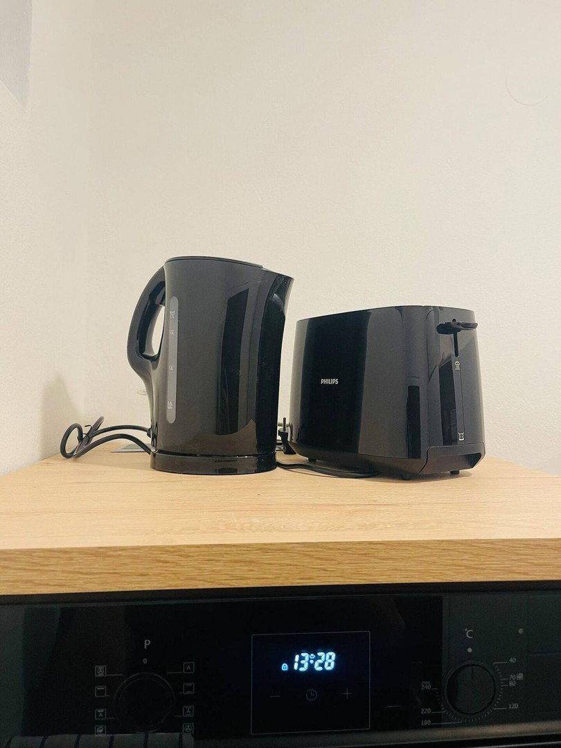 Schwarzer Wasserkocher und Toaster auf einer Holzarbeitsplatte über einem Backofen.