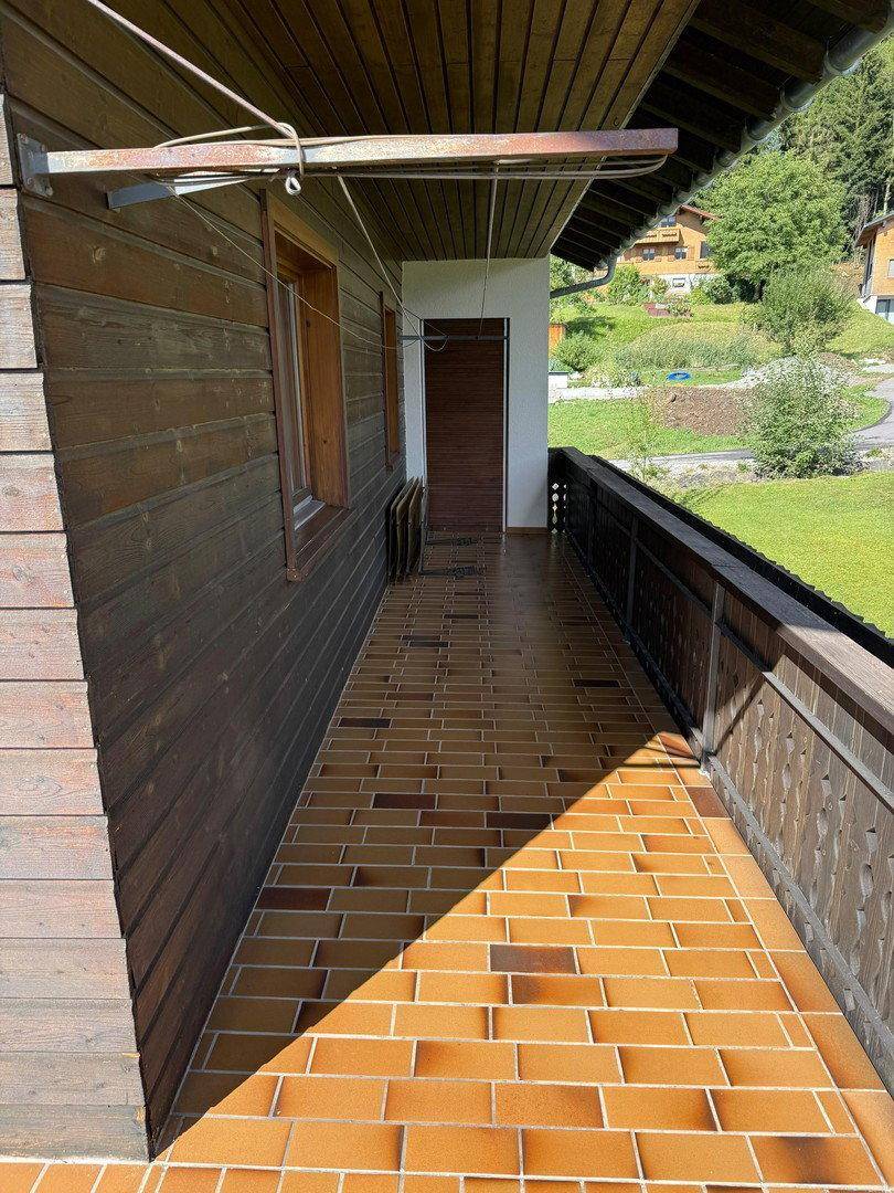 Langer Balkon mit Holzverkleidung und braunen Fliesen, ideal für sonnige Stunden.