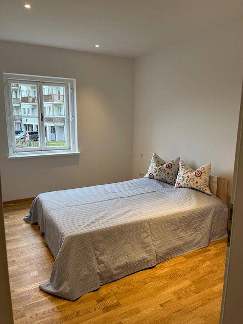 Helles Schlafzimmer mit Holzboden und einem Doppelbett, das auf die Straße blickt.