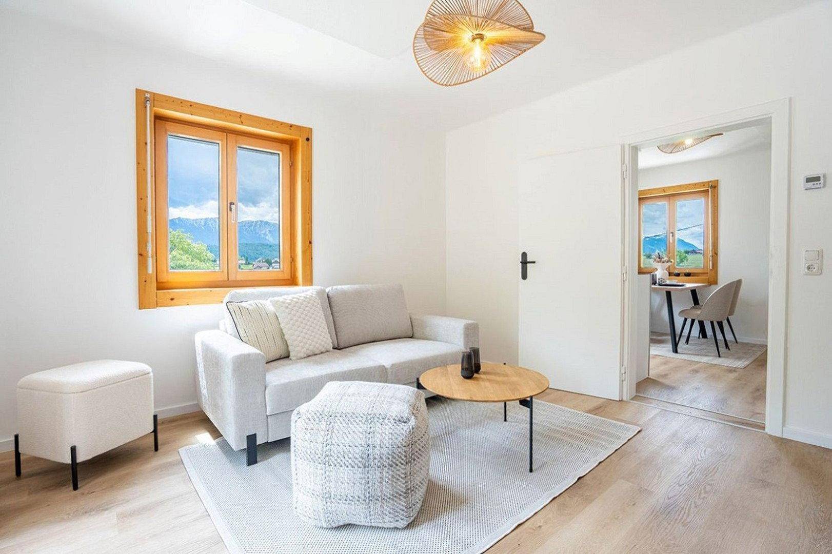 Helles Wohnzimmer mit modernem Sofa, Holzboden und weitem Blick auf die Landschaft.
