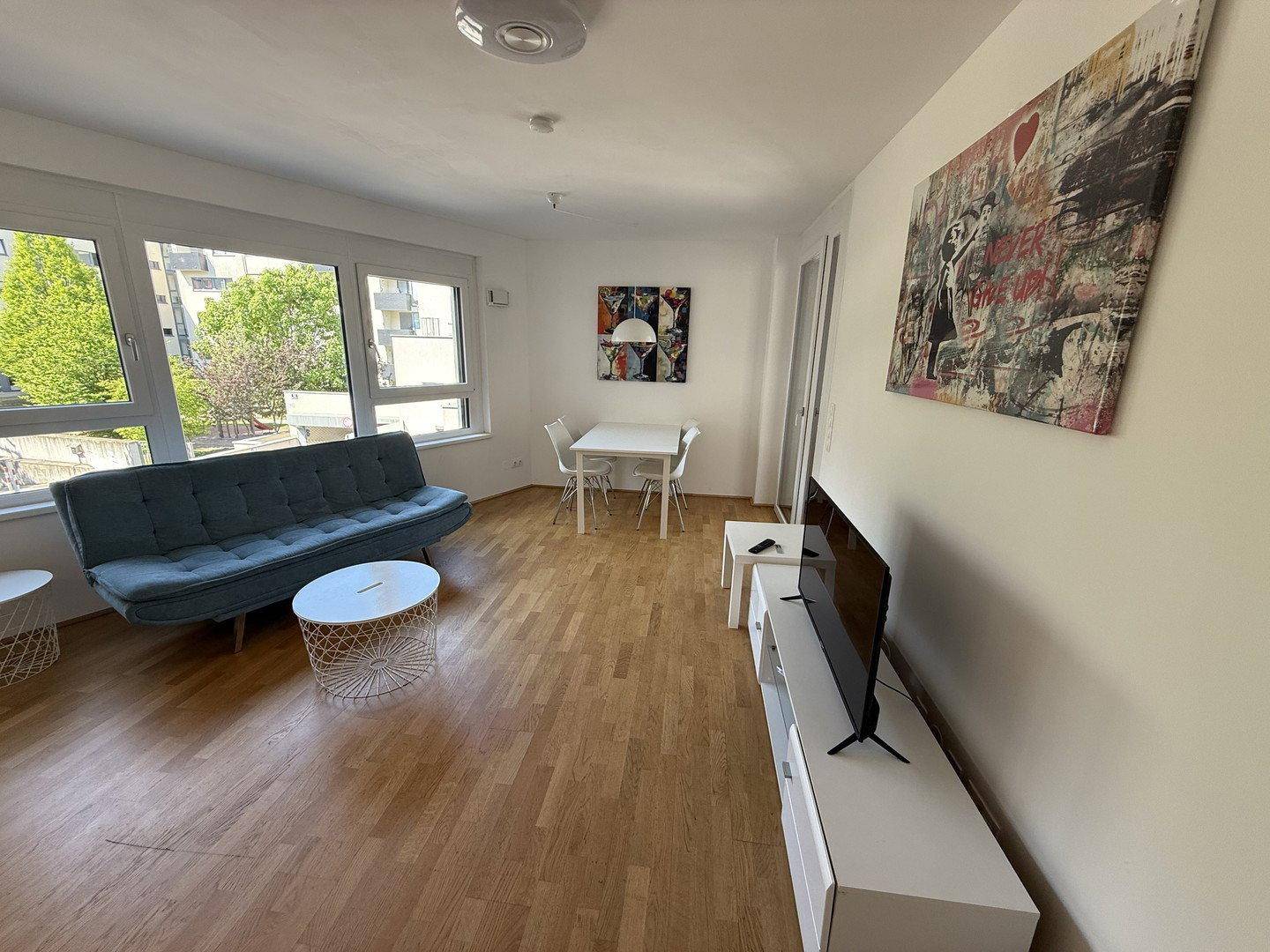 Geräumiger Wohnbereich mit Holzboden, moderner Einrichtung und viel Tageslicht durch große Fenster.