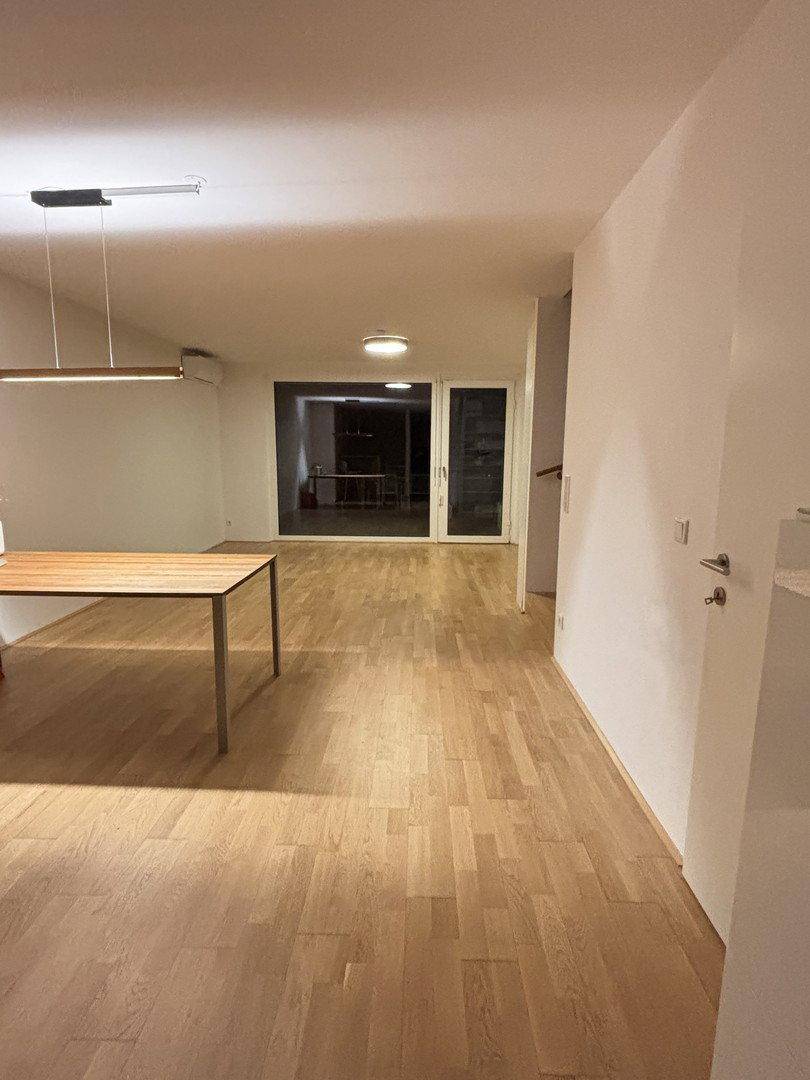 Geräumiger Wohn-Essbereich mit hellem Holzfußboden und großen Fenstern, die viel Licht hereinlassen.
