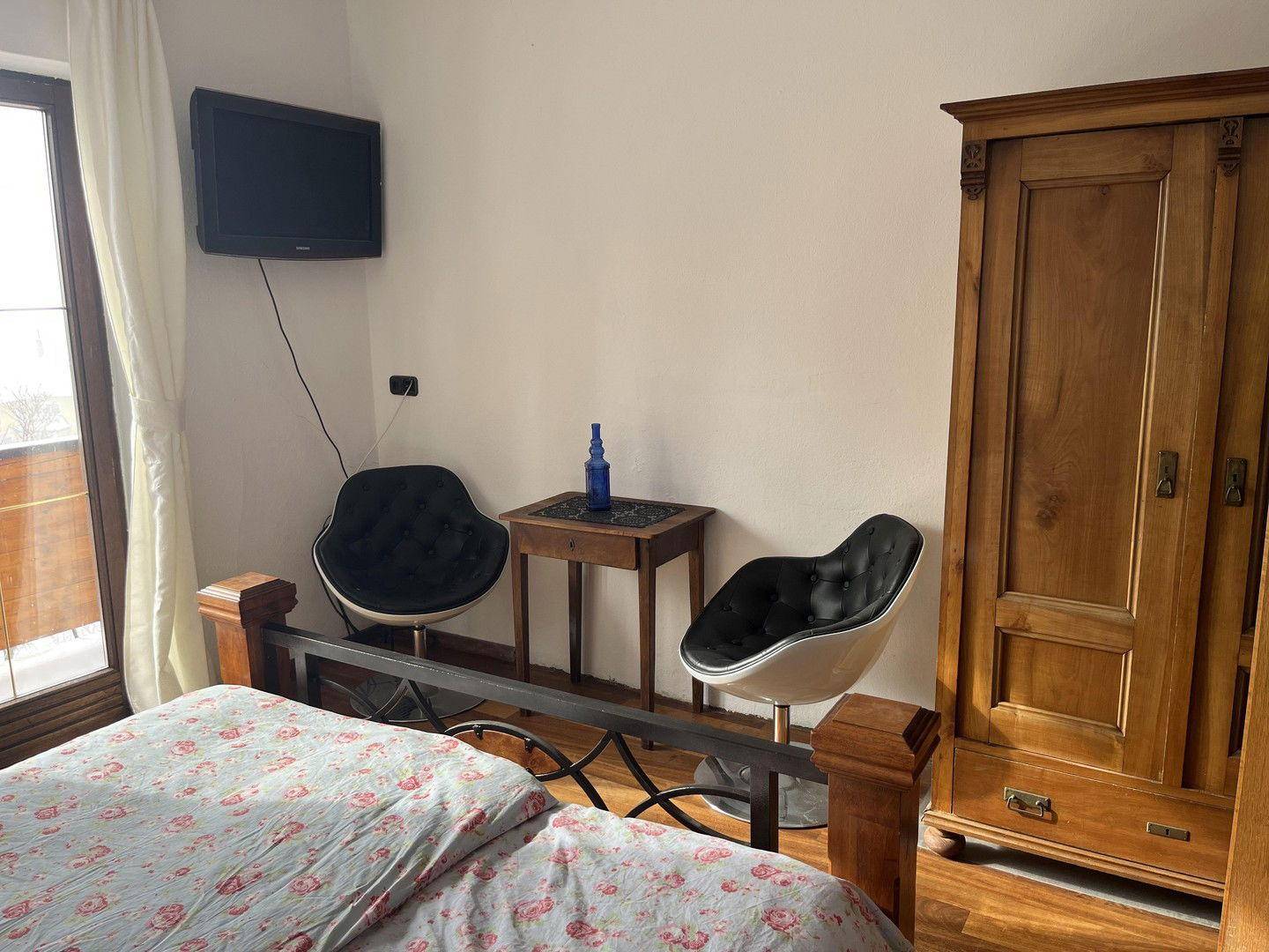 Schlafzimmer mit Holzschrank, Fernseher und modernen Stühlen, mit Blick nach draußen.