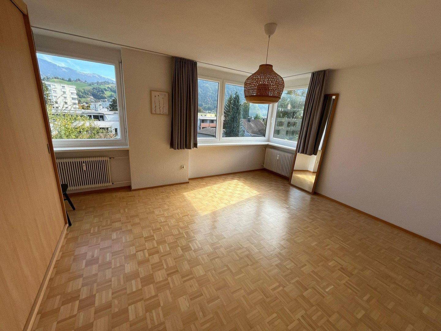 Geräumiges Schlafzimmer mit Parkettboden, großen Fenstern und viel natürlichem Licht sowie Bergblick.