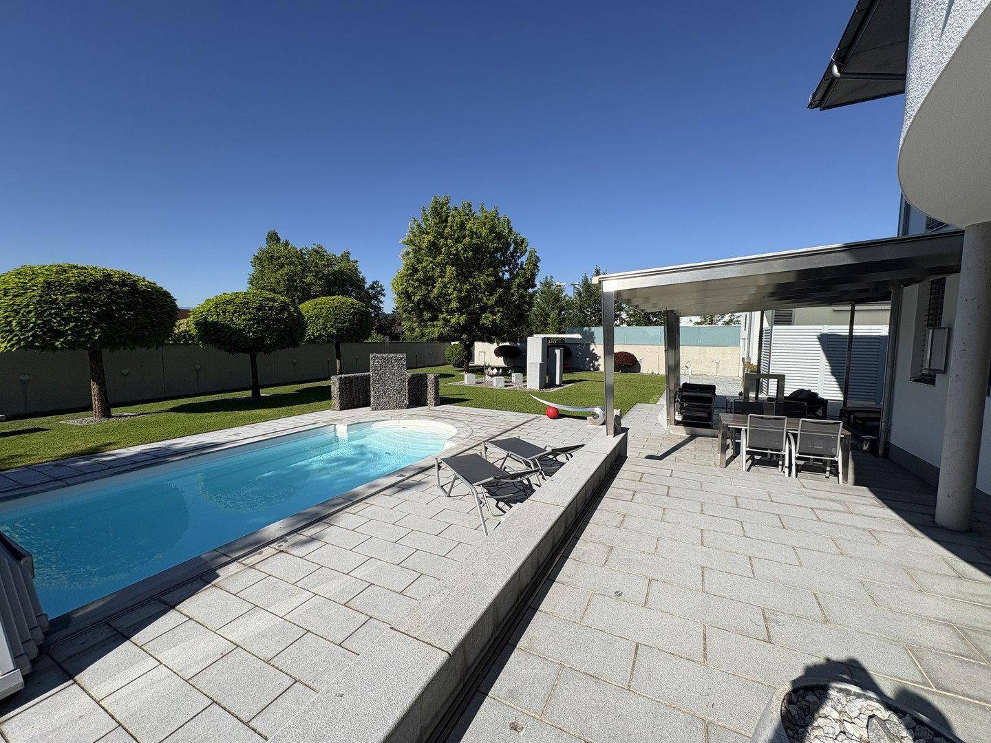 Großzügige Terrasse mit Swimmingpool, Sonnenliegen und Essbereich unter einer modernen Pergola.