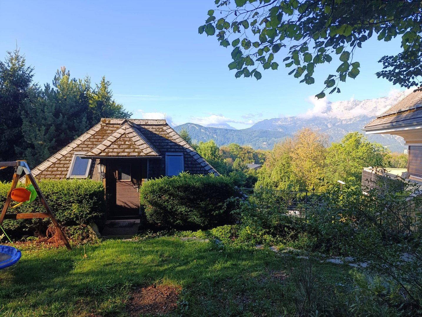 Haus mit Garten, Schaukel und Blick auf die umliegende grüne Landschaft und Berge.