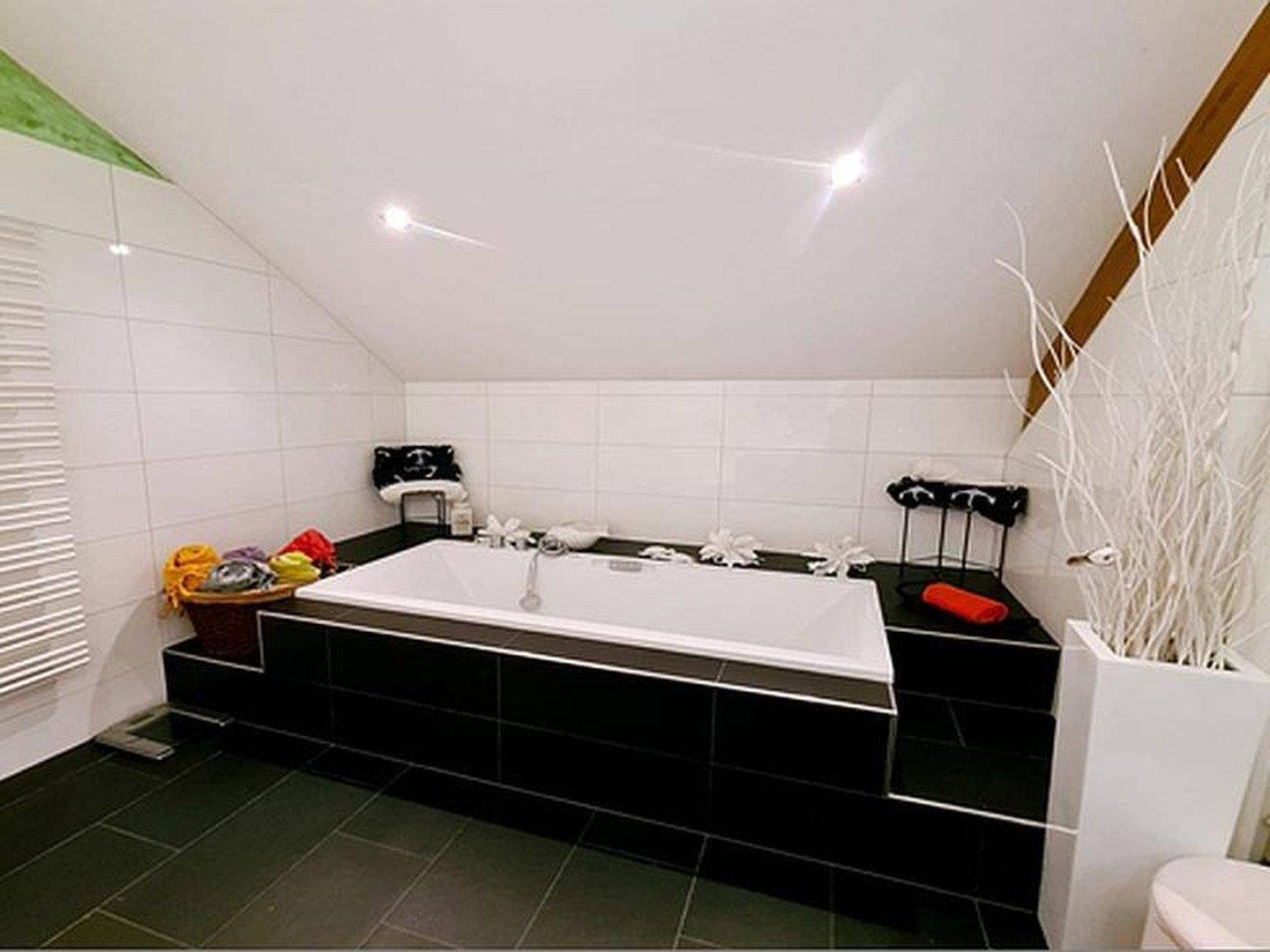 Großes Badezimmer mit eingebauter Badewanne, dunklen Fliesen und Dachschräge.