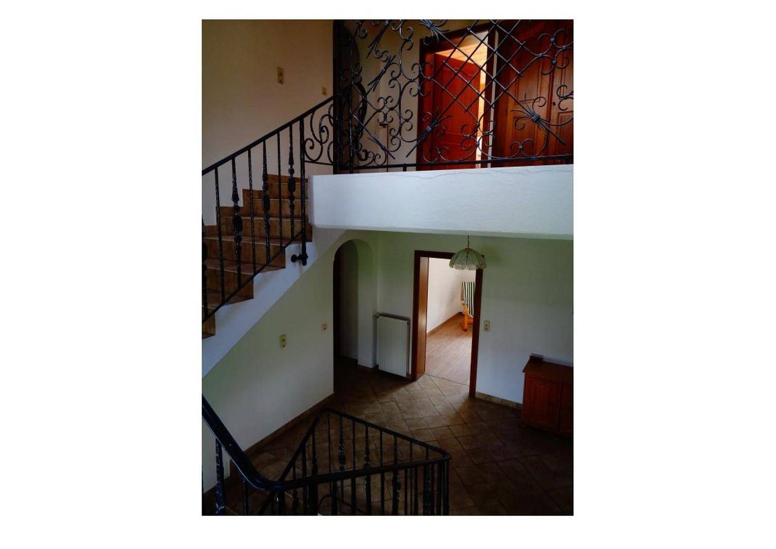 Geräumiges Treppenhaus mit schmiedeeisernem Geländer und Zugang zu verschiedenen Ebenen des Hauses.