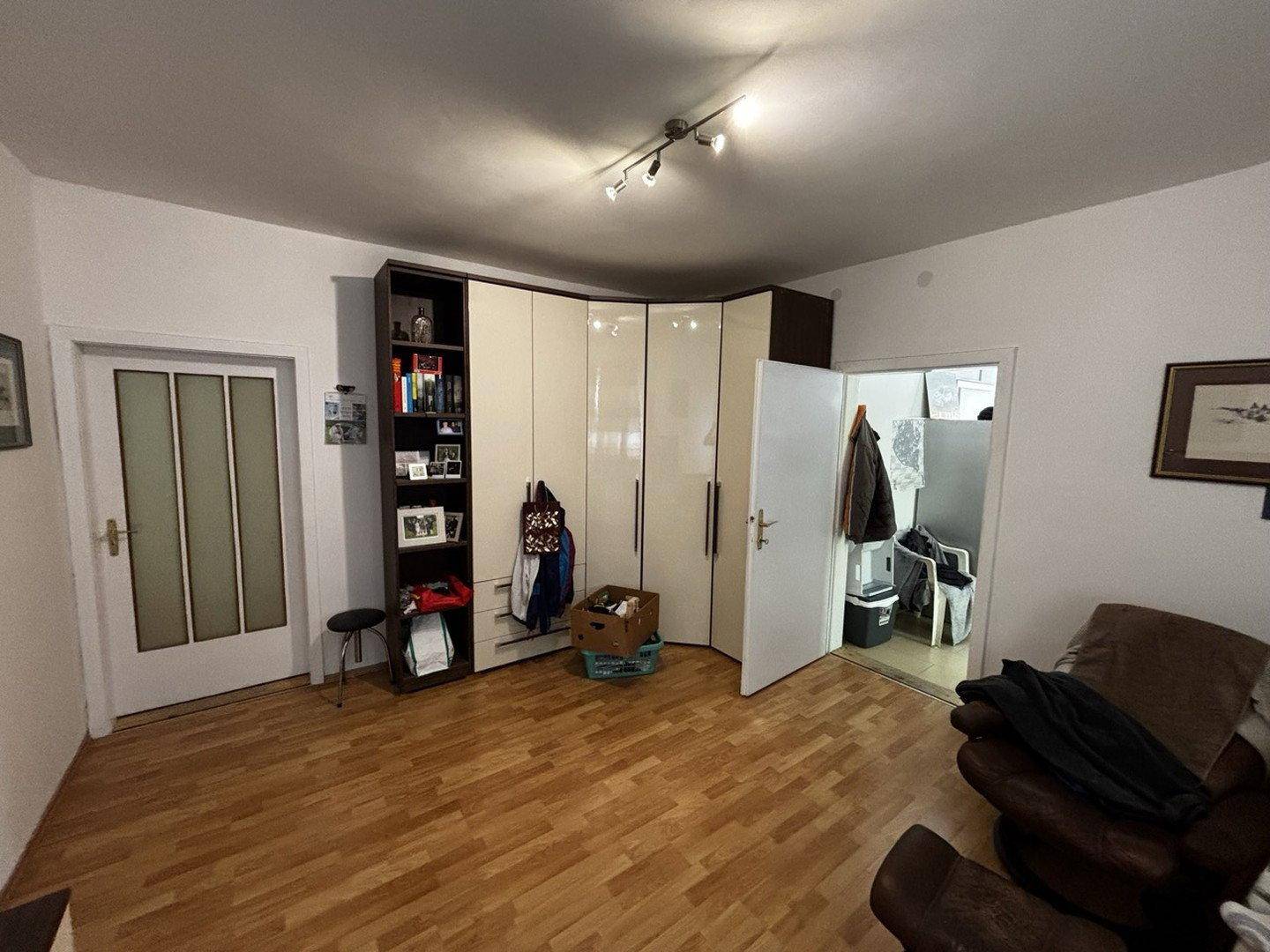 Heller Raum mit Holzfußboden, großem Kleiderschrank und Zugang zu einem weiteren Bereich.