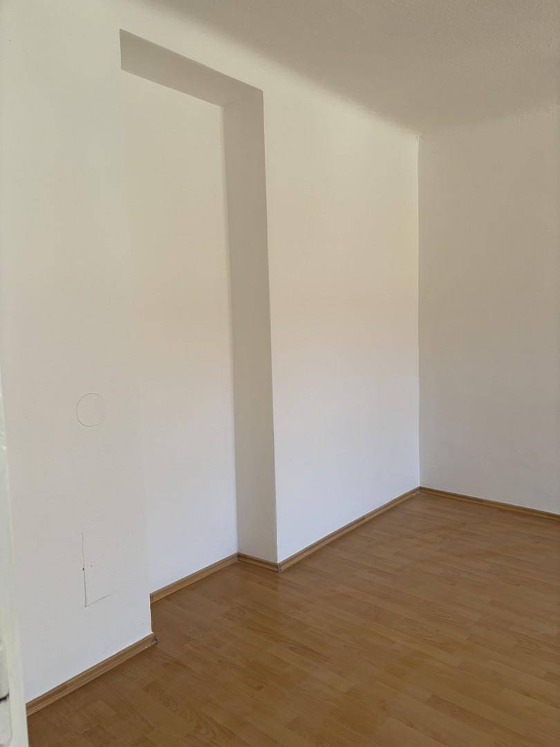 Leeres Zimmer mit weißen Wänden und hellem Holzfußboden, bereit zur individuellen Gestaltung.