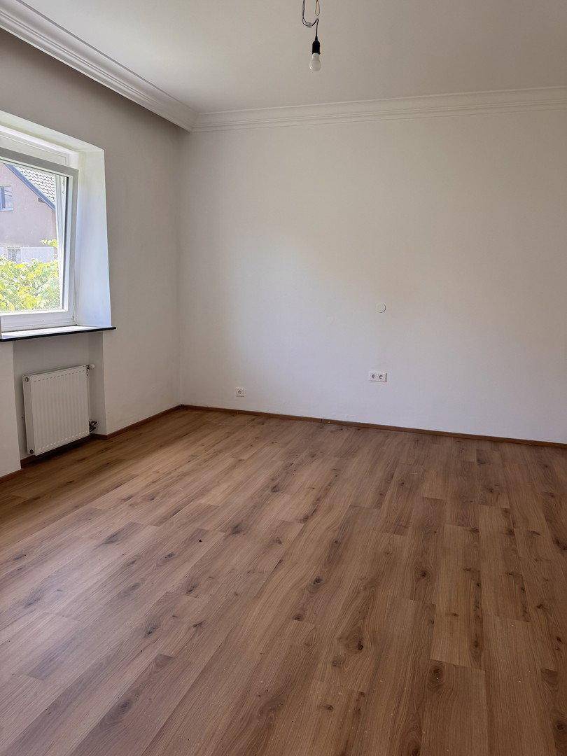 Heller Raum mit Holzboden, einem Fenster und weißen Wänden, bereit zur individuellen Gestaltung.