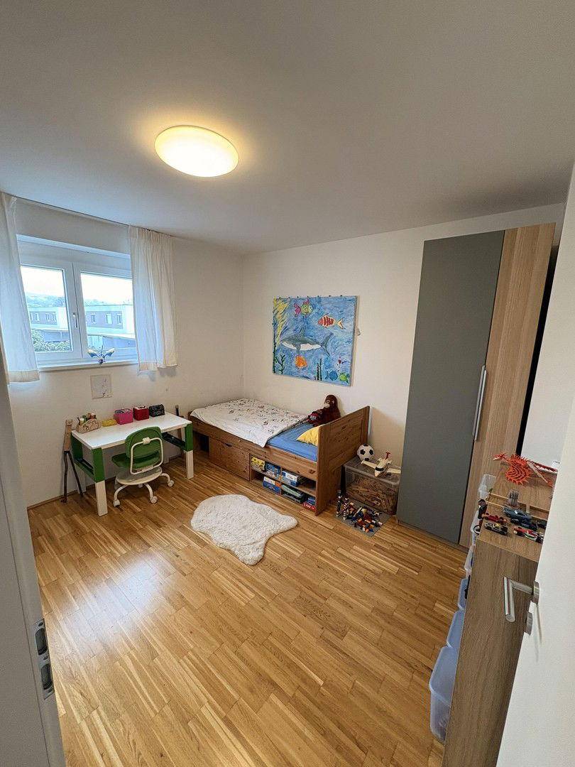 Kinderzimmer mit Holzboden, Schreibtisch und einem Bett mit Stauraum.