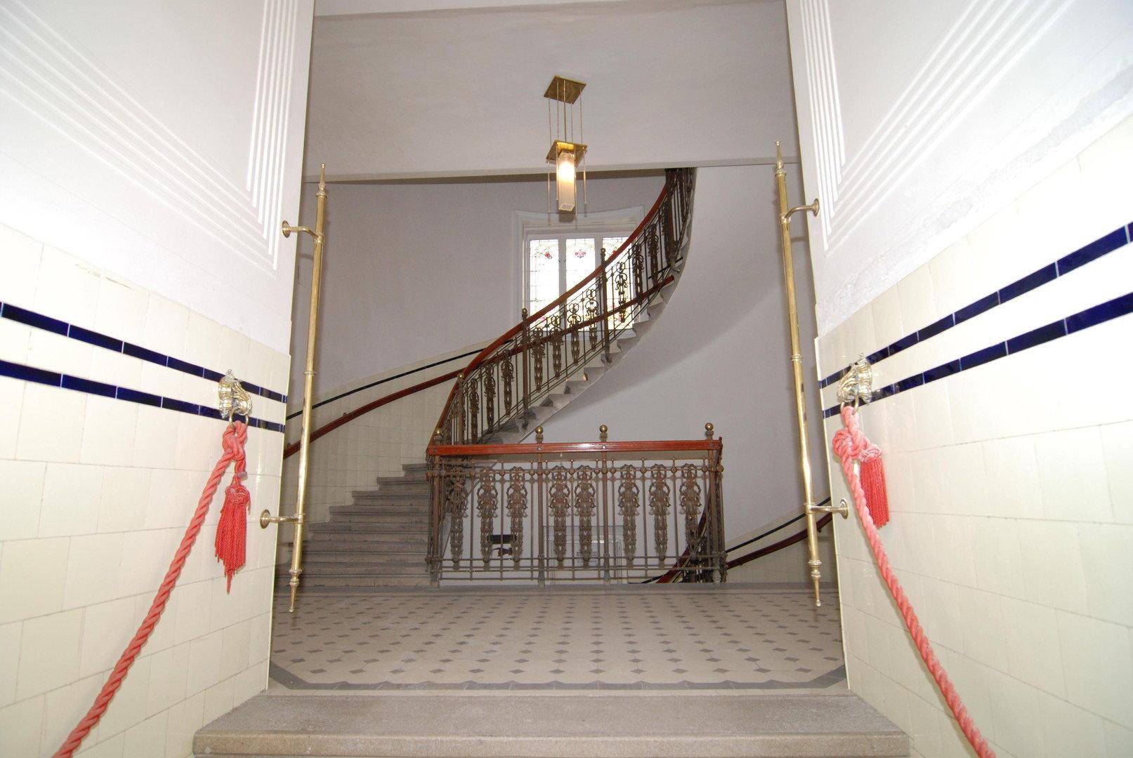 Prunkvolles Treppenhaus mit geschwungener Holztreppe, kunstvollem Geländer und dekorativem Fliesenboden.